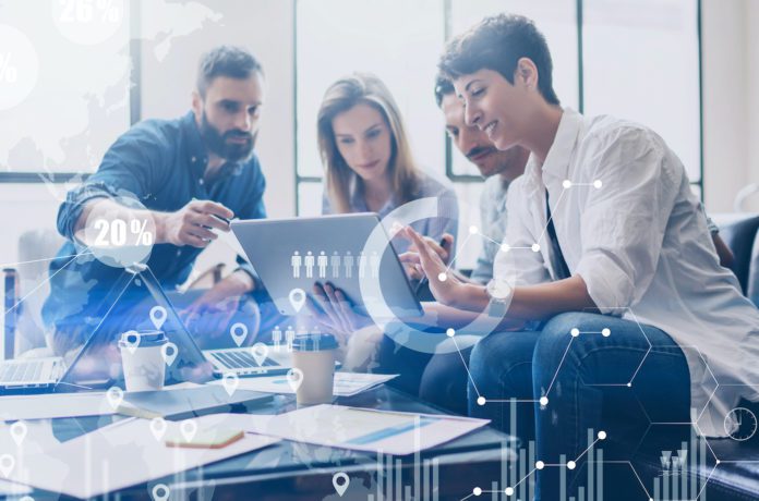 Employees meet around table and over laptop computer.